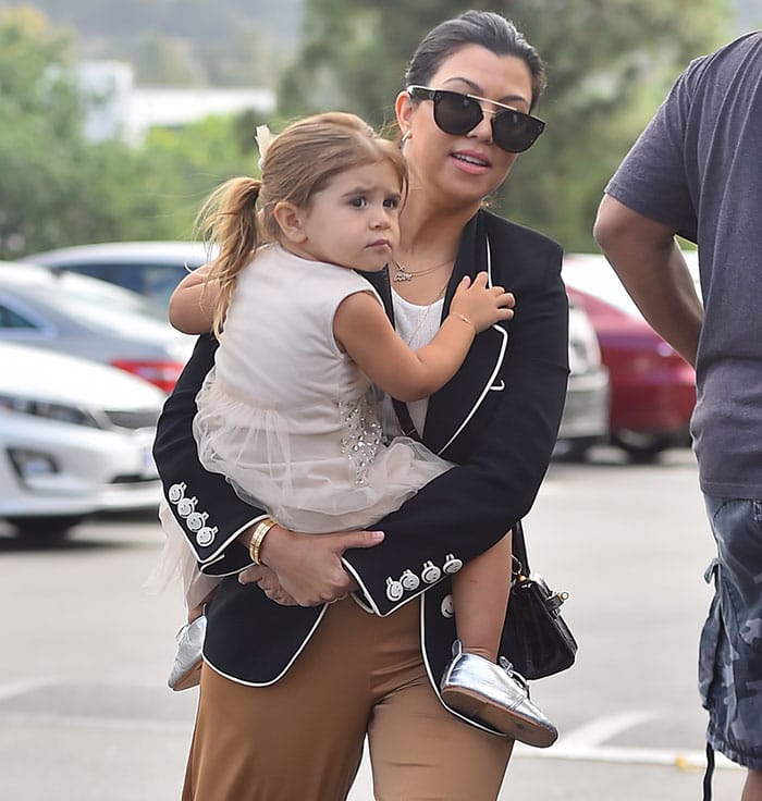 Kourtney Kardashian's daughter, Penelope Disick, looks adorable in a cream-colored sleeveless dress adorned with delicate embellishments and a layered tulle skirt, perfectly paired with shiny metallic silver shoes for a charming and festive touch