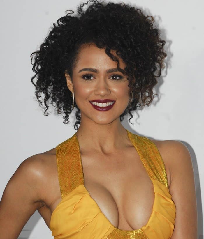 Nathalie Emmanuel styled her marigold deep scoop dress with a beaded collar and bold, deep red lipstick, complemented by her natural curly hair and delicate hoop earrings