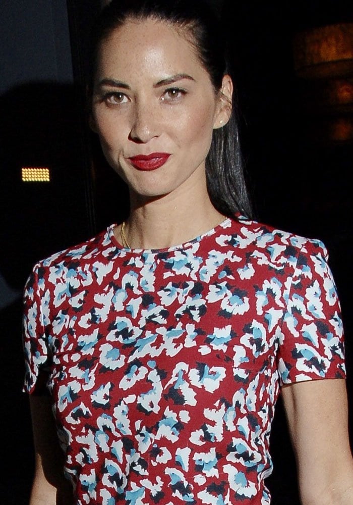 Olivia Munn complements her vibrant floral romper with a slicked-back ponytail and bold red lipstick, creating a fresh and elegant look