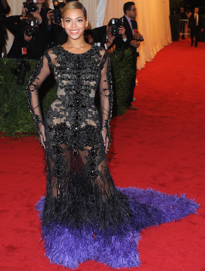 Beyoncé stuns on the red carpet at the 2012 Met Gala in a sheer black and purple feathered Givenchy gown, adorned with intricate crystal embellishments and embroidery