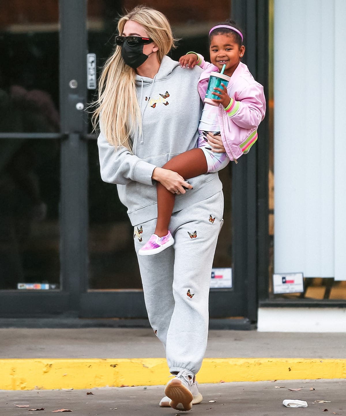 Wearing butterfly-embroidered sweatpants and a matching pullover hoodie by U.S streetwear company FELT, Khloé Kardashian carries her tall daughter True Thompson