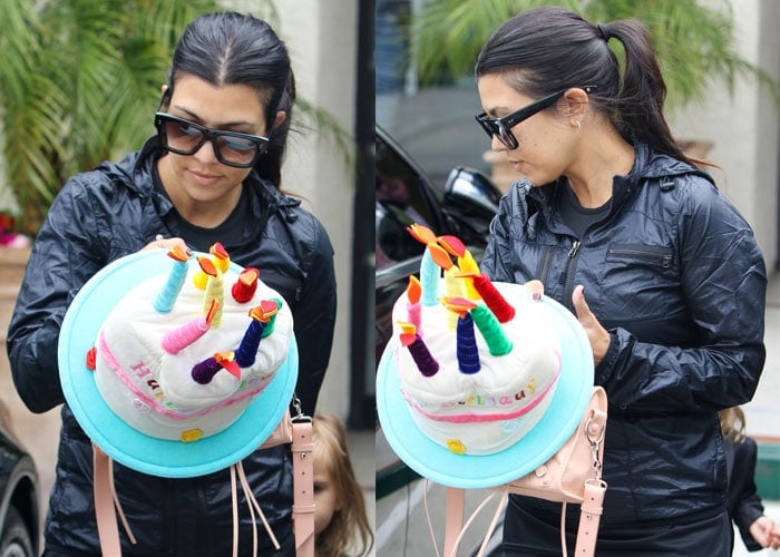 Kourtney Kardashian carrying a Happy Birthday cake decoration