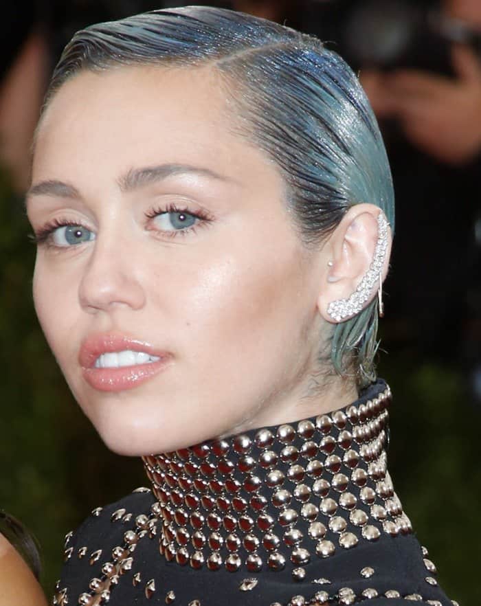 Miley Cyrus rocks a sleek, blue-tinted, slicked-back hairstyle paired with a bold ear cuff and natural makeup