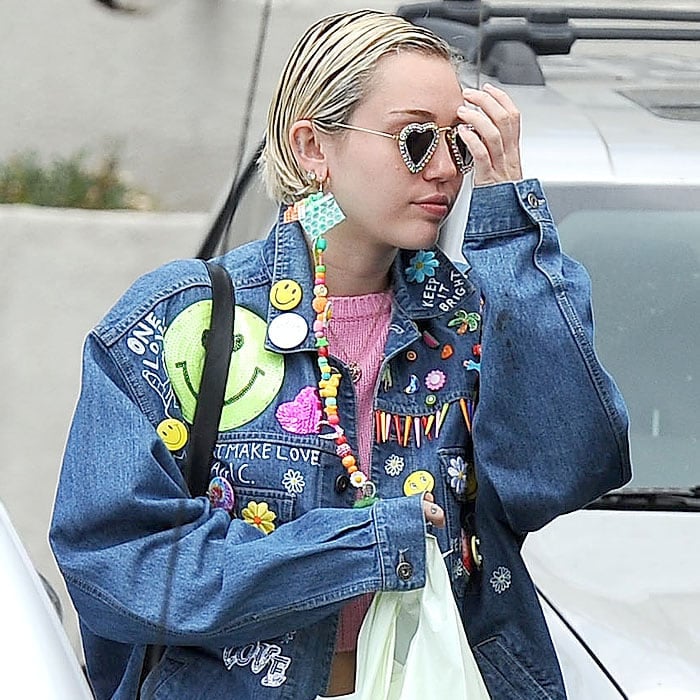 Miley Cyrus rocking heart-shaped sunglasses, a long dangling earring, and an embellished denim jacket