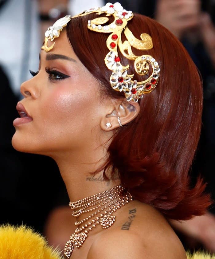 Rihanna captivates with an intricate gold and jeweled crown, complementing her sleek red hair and layered gold necklace at the 2015 Met Gala