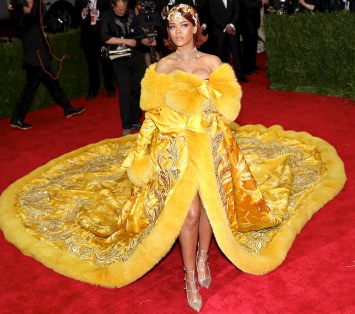 Rihanna poses confidently in a regal yellow Guo Pei gown, complete with an opulent fur-trimmed train and intricate embroidery, at the 2015 Met Gala