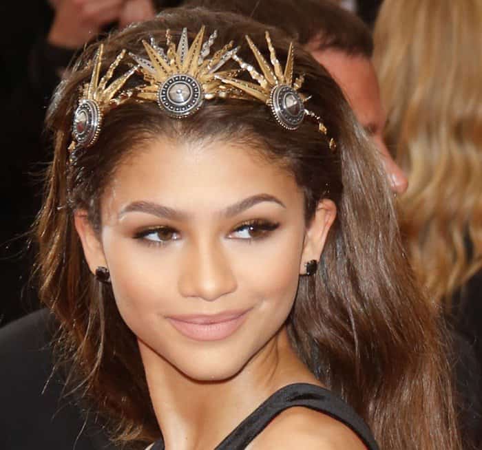 Zendaya shines with a sleek hairstyle adorned with a stunning gold and jewel-encrusted headpiece, complemented by natural makeup and perfectly sculpted brows at the 2015 Met Gala