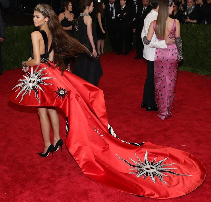 Zendaya dazzles in a striking Fausto Puglisi gown featuring a black velvet bodice, a high-low crimson silk skirt adorned with hand-embroidered sun motifs, and a dramatic train at the 2015 Met Gala