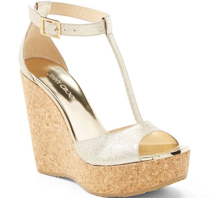 Embossed goldtone hardware adorns the toe of a fierce T-strap sandal elevated on a towering cork wedge.