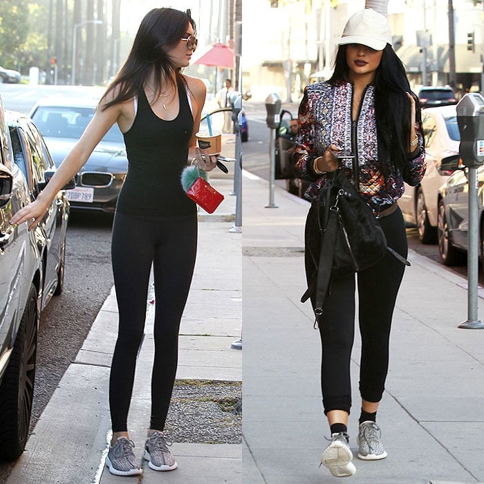 Kendall and Kylie Jenner both sport athleisure outfits comprised of black tank tops, black leggings, and black-and-gray sneakers