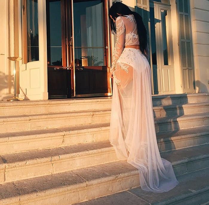 Kylie Jenner poses on the steps in a sheer Francesco Scognamiglio outfit, showcasing intricate floral appliqués and a flowing train