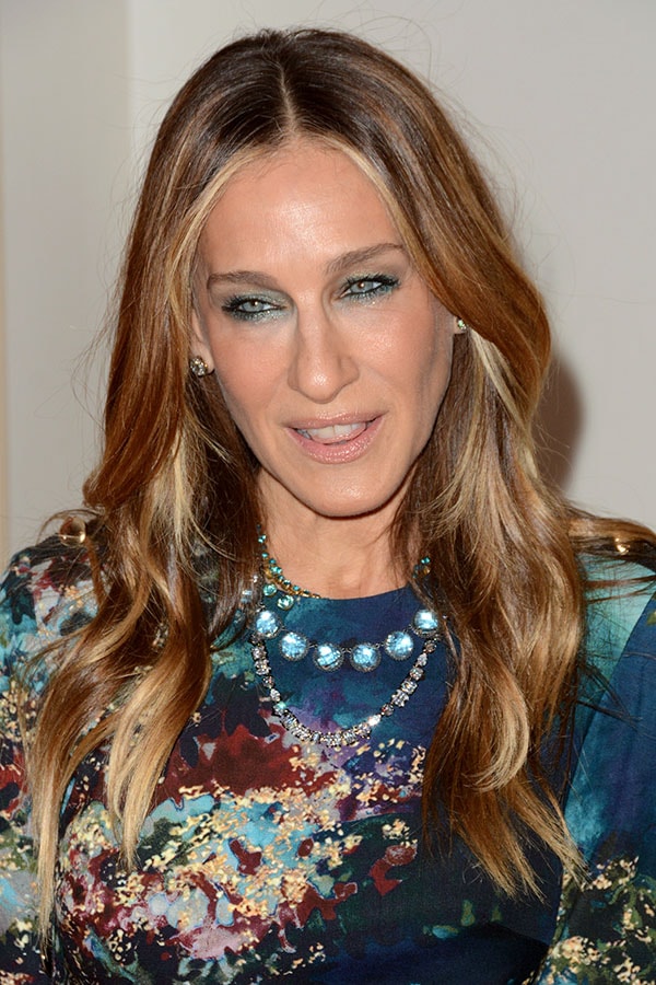 Sarah Jessica Parker wearing layered jewel necklaces and shimmery blue eye makeup that matches her blue patterned dress