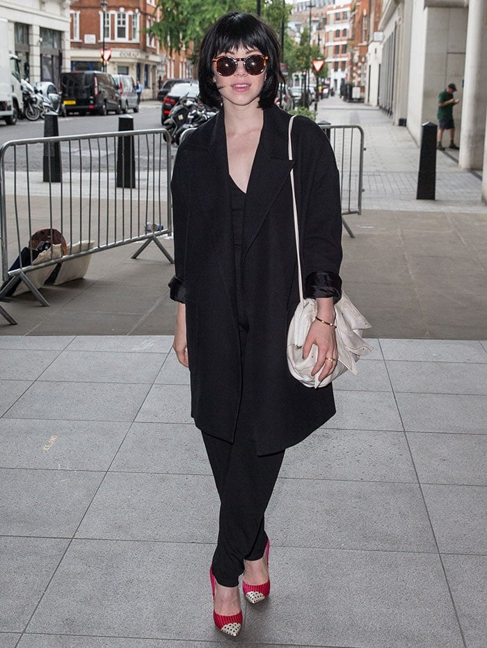 Carly Rae Jepsen in a black V-neck jumpsuit partially concealed under a thick black coat