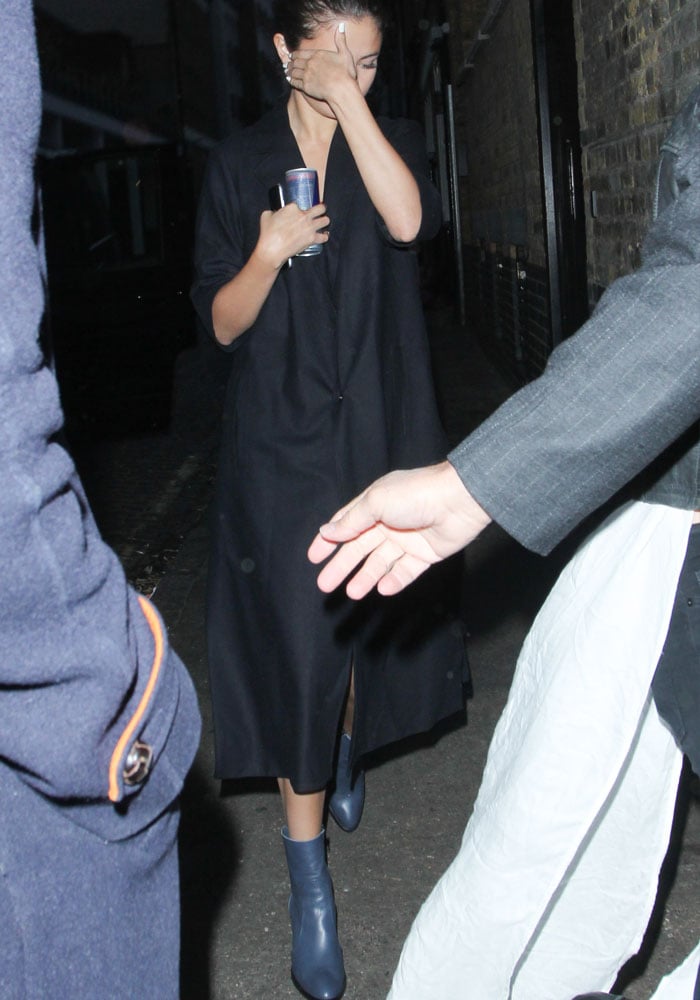 Selena Gomez clutches the essentials — a phone and a can of Red Bull — in one hand while hiding her face with the other