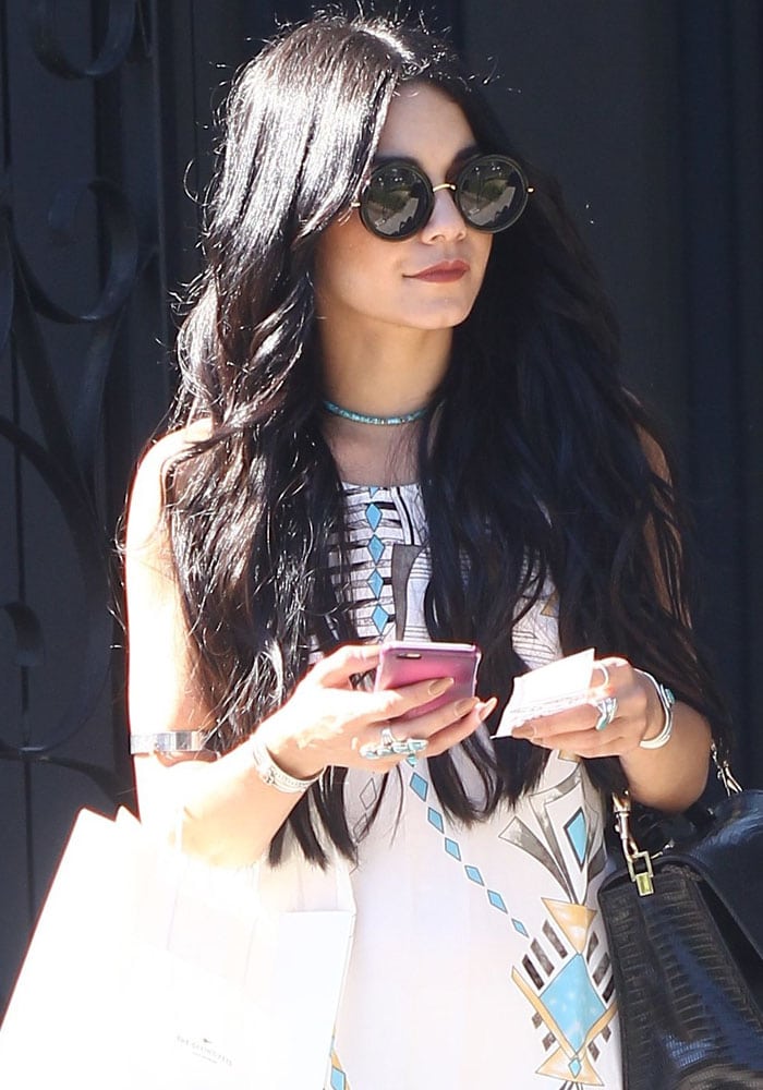 Vanessa Hudgens exudes boho-chic style in a printed sleeveless dress, layered silver jewelry, round sunglasses, and a black handbag, perfectly capturing her signature laid-back glamour