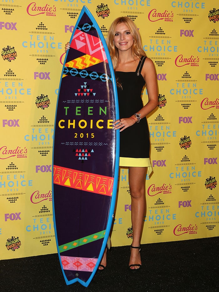 Bella Thorne celebrates her win at the 2015 Teen Choice Awards, proudly holding her surfboard trophy while wearing a black Alexander Wang mini dress and matching ankle-strap sandals