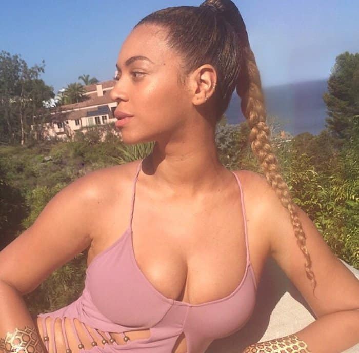 Beyoncé looks radiant in a sunlit outdoor setting, showcasing her elegant style with a sleek braided ponytail and a stylish pink top