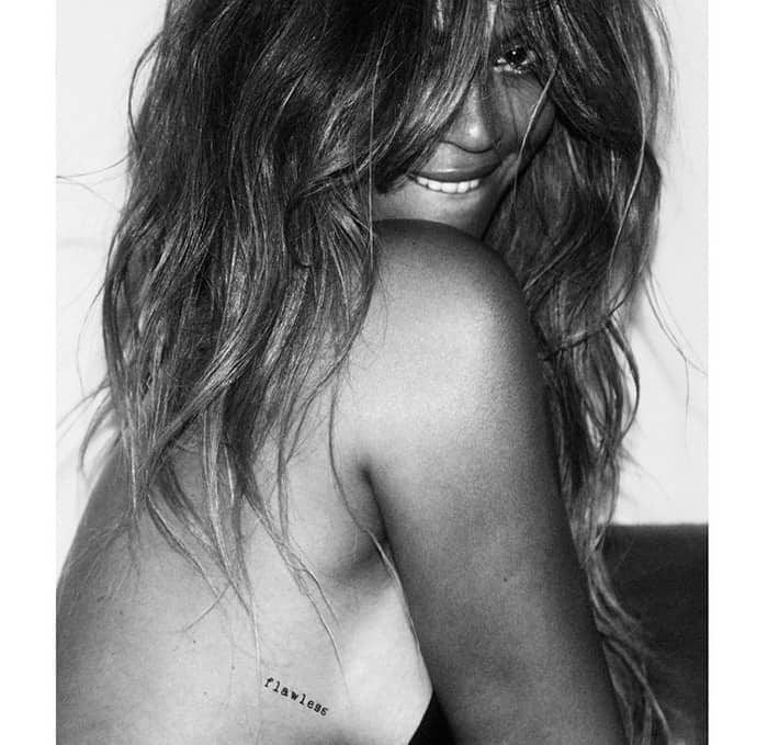 Beyoncé gives a playful smile while showing off a small "flawless" tattoo on her side, perfectly capturing her confident and effortless style