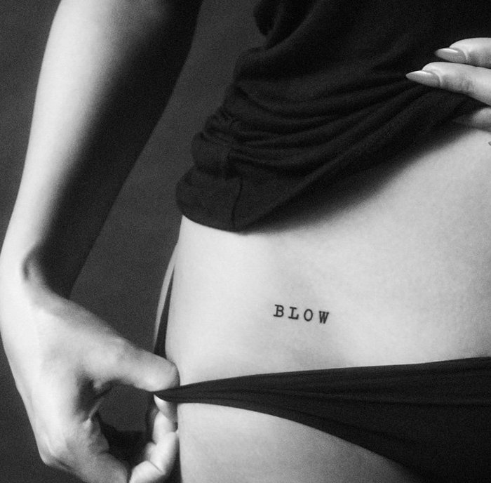 A close-up shot reveals a bold "BLOW" flash tattoo placed just above the hip, accentuated by the subtle pull of fabric, adding a provocative and stylish edge to the look