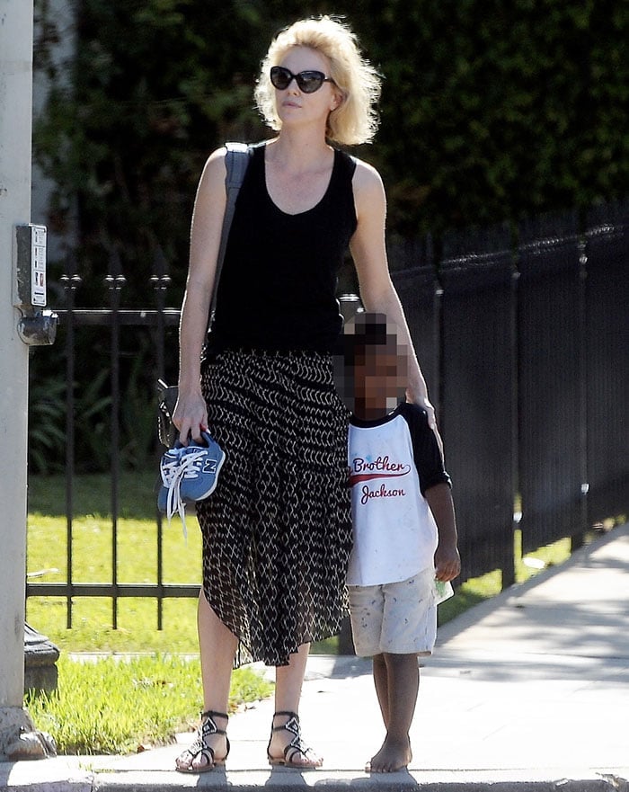 Charlize Theron holds her son Jackson's shoes as the two pause on a sidewalk