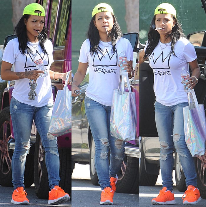 Christina Milian pops a vape pen into her mouth as she sports a pair of bright orange Reebok sneakers