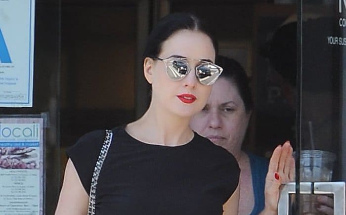 Dita Von Teese showcases her signature elegance with cat-eye sunglasses and bold red lips, adding a glamorous touch to her casual outfit