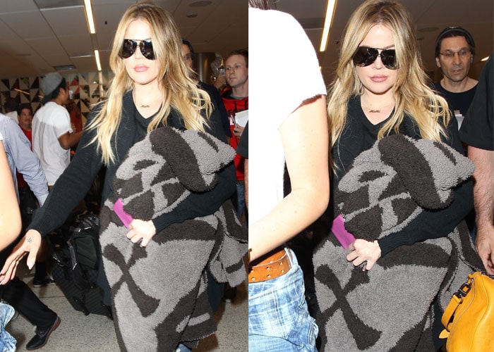 Khloe hides her eyes behind aviators and holds what appears to be a large blanket as she strolls through LAX