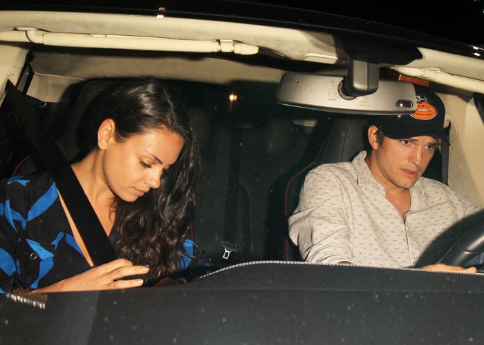 Mila Kunis lets her long dark hair fall over her shoulder and in front of her chevron-printed dress as she sits in a car with husband Ashton Kutcher