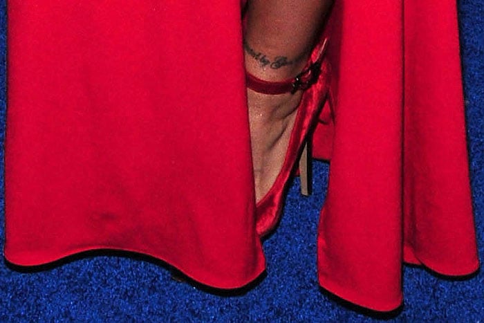 Red velvet ankle-strap pumps peeking out from the thigh-high split on Ronda Rousey's red gown