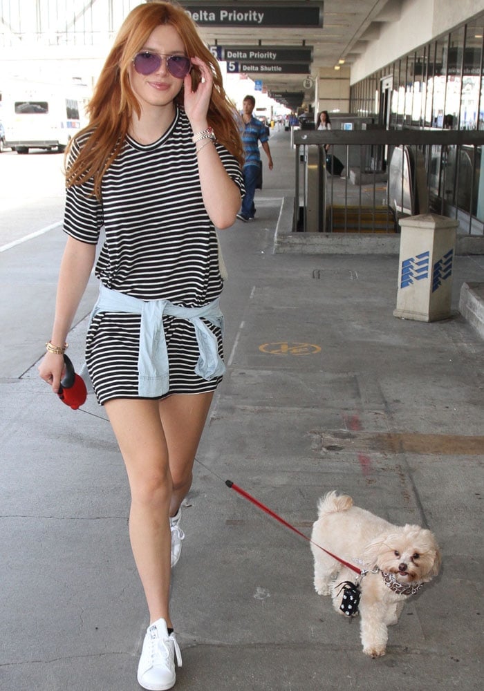 Bella Thorne adjusts her aviator sunglasses as she walks her pet dog through the Los Angeles airport