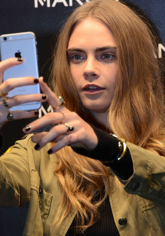 Cara Delevingne flashes her finger tattoos as she holds up an iPhone