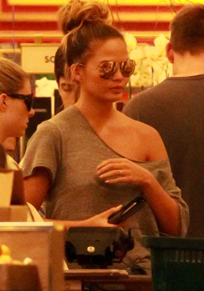 Chrissy Teigen wears a pair of aviator sunglasses and holds her wallet