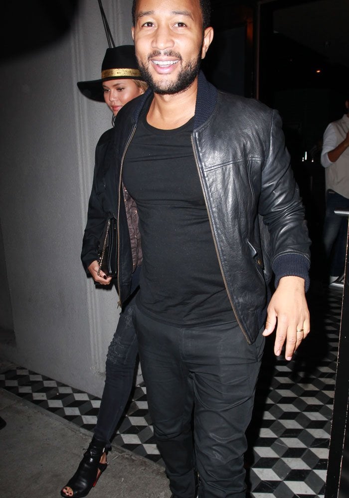 Chrissy Teigen and John Legend step out in coordinated all-black looks for a stylish date night, with Chrissy in Louboutin heels and a wide-brim hat and John in a sleek leather jacket and black tee