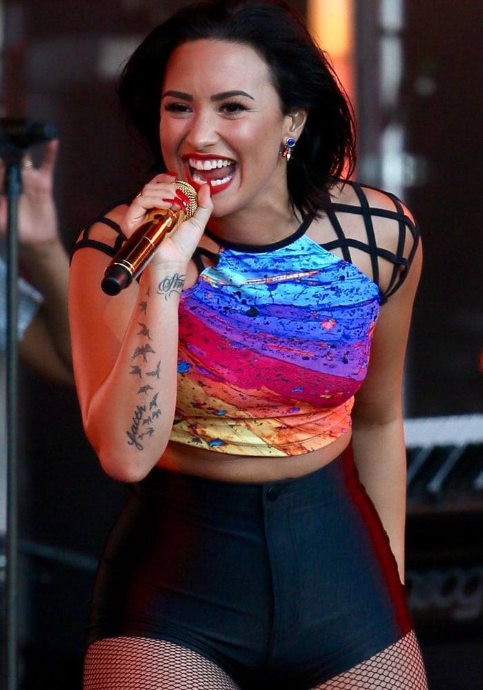 With a tattoo of flying birds on her right forearm, Demi Lovato performs in front of a live audience