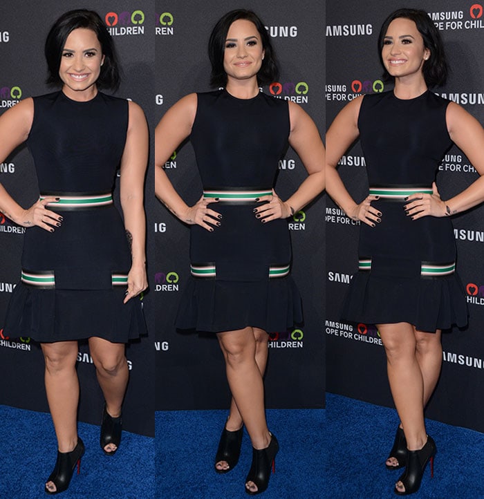 Demi Lovato smiles on the blue carpet in an LBD