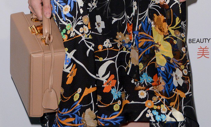 Diane Kruger carries the structured “Grace” large trunk bag by Mark Cross, crafted from nude saffiano leather with gold-tone hardware for a vintage-inspired finish