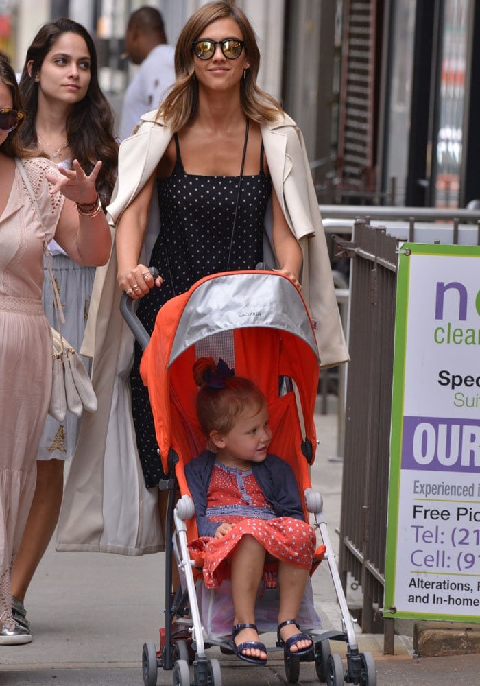 Jessica Alba flings a khaki coat over her shoulders as she takes a stroll in a polka-dot dress