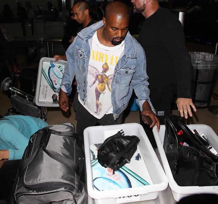 Kanye West goes through security at LAX in a denim jacket and printed white t-shirt