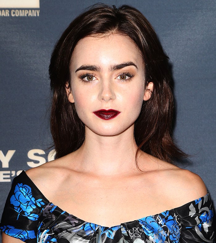 Lily Collins stuns with her glossy loose waves and bold gothic makeup featuring dark berry lipstick and defined brows