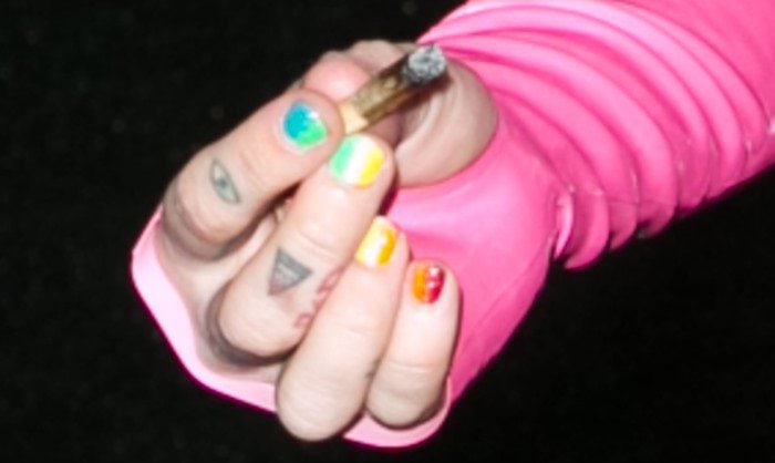 Miley Cyrus holds out a joint and shows off her finger tattoos and multi-colored nails