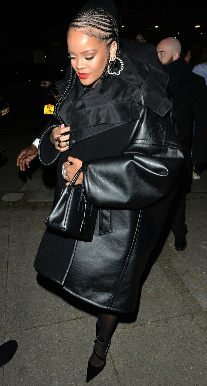 Rihanna steps out in style, sporting a sleek black faux leather coat, braided hair, and bold red lipstick while carrying a Prada Galleria mini tote