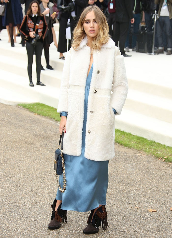 Suki Waterhouse wears an ankle-length blue dress and a white fleece coat as she attends Fashion Week