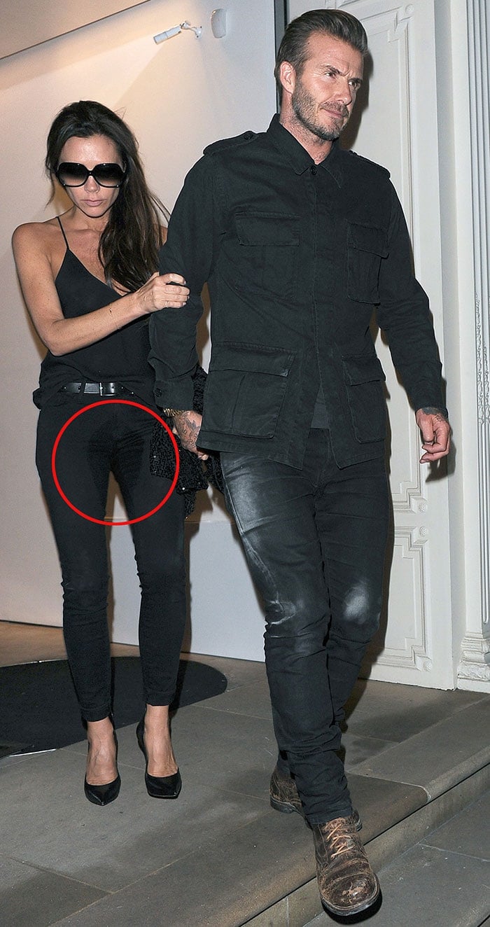 Victoria Beckham clutches onto the arm of her husband, David Beckham, as a large crotch stain is clearly visible on her all-black outfit