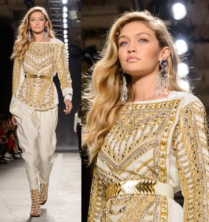 Gigi Hadid radiates in a gold-embellished Balmain x H&M ensemble, pairing intricate beadwork with statement crystal earrings for a regal runway presence