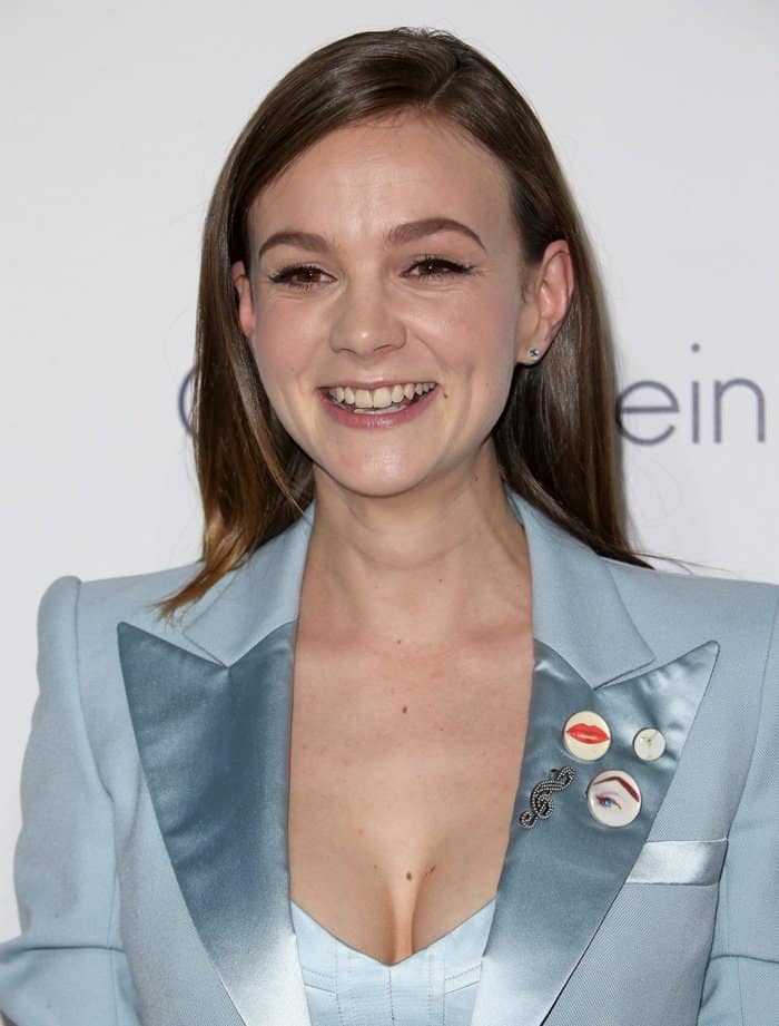 Carey Mulligan radiates elegance in her powder blue Marc Jacobs pantsuit, complemented by playful pins on the lapel and a subtle hint of cleavage