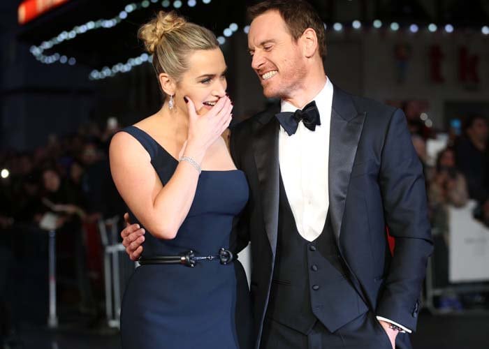 Kate Winslet touches her face and laughs with co-star Michael Fassbender at the premiere of "Steve Jobs"