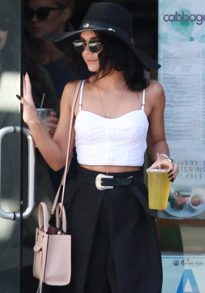 Vanessa Hudgens wears a wide-brimmed hat over her hair and carries a drink as she orders lunch to go