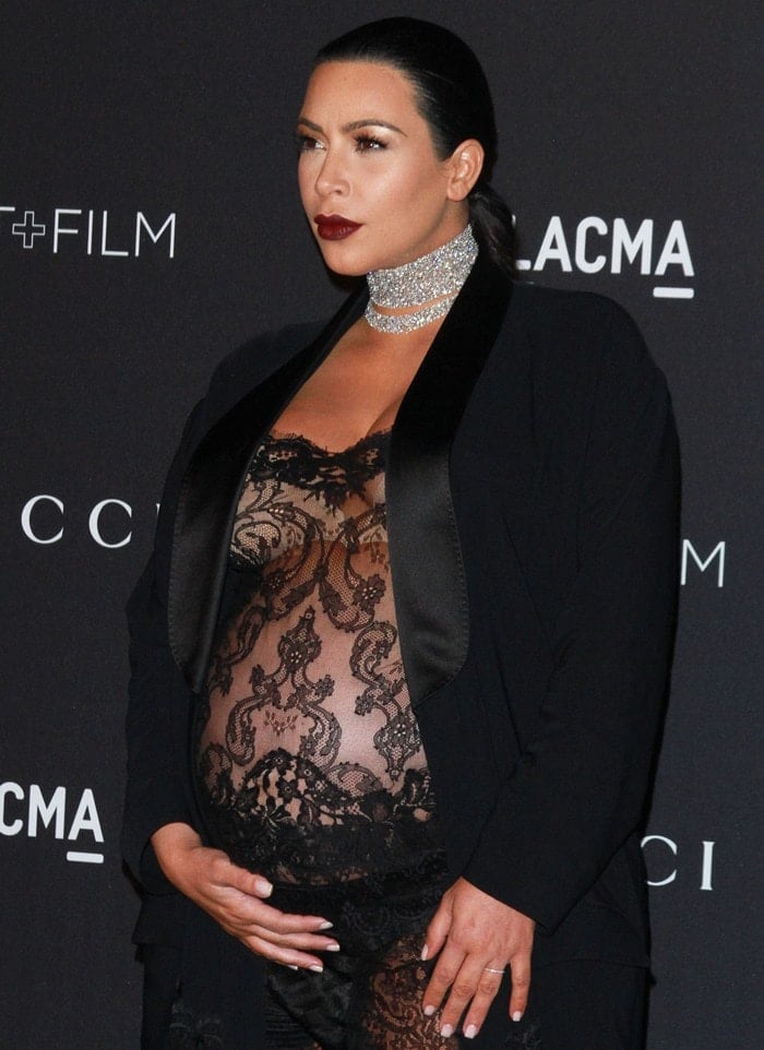 Kim Kardashian stuns in a sheer black lace jumpsuit paired with a tailored satin blazer, showcasing her baby bump with elegance