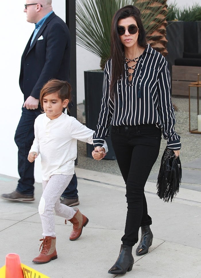 Mason Dash Disick wearing a white long-sleeved top, gray tracksuit pants, and tan boots