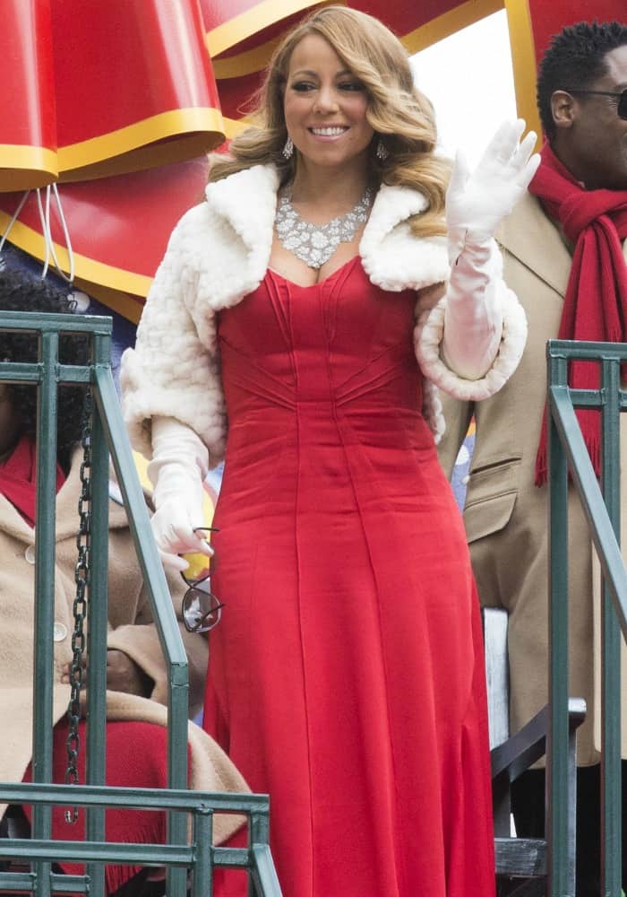 Mariah Carey waves to the crowd in a stunning red gown paired with a cozy white shrug and elegant accessories at the Macy's Thanksgiving Day Parade